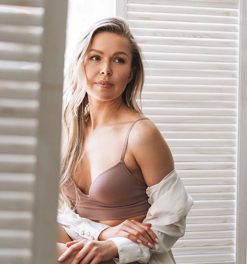 Blonde woman in a pink tank top, sitting by her window sill - Scar Revision in New York, NY